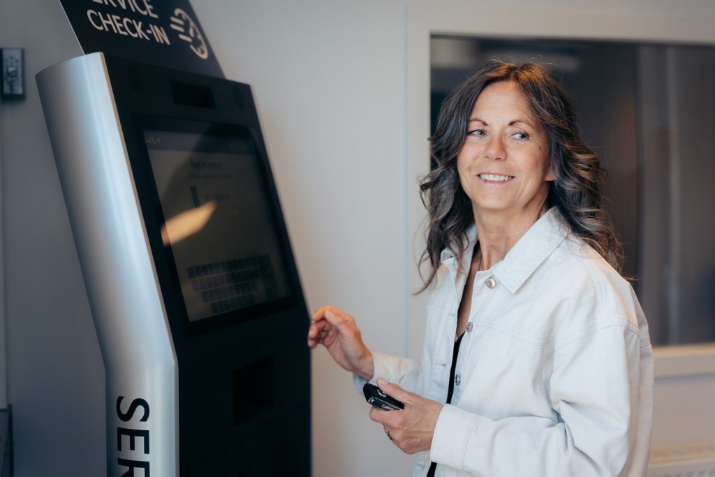 Kvinna använder Tjekvik självbetjäningsstation för Kia service i en modern bilverkstad.
