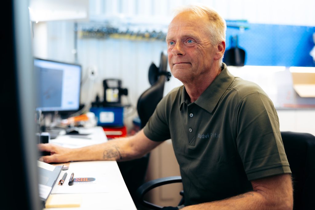 Anders från Rudvi Fritid sitter vid sitt skrivbord och arbetar framför en datorskärm. Han bär grön pikétröja med Rudvi Fritid-logga.